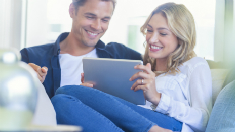 A young couple on a tablet device happy they’ve found a unique margin loan with the added benefit of a repayment plan that helps them save for a home deposit.